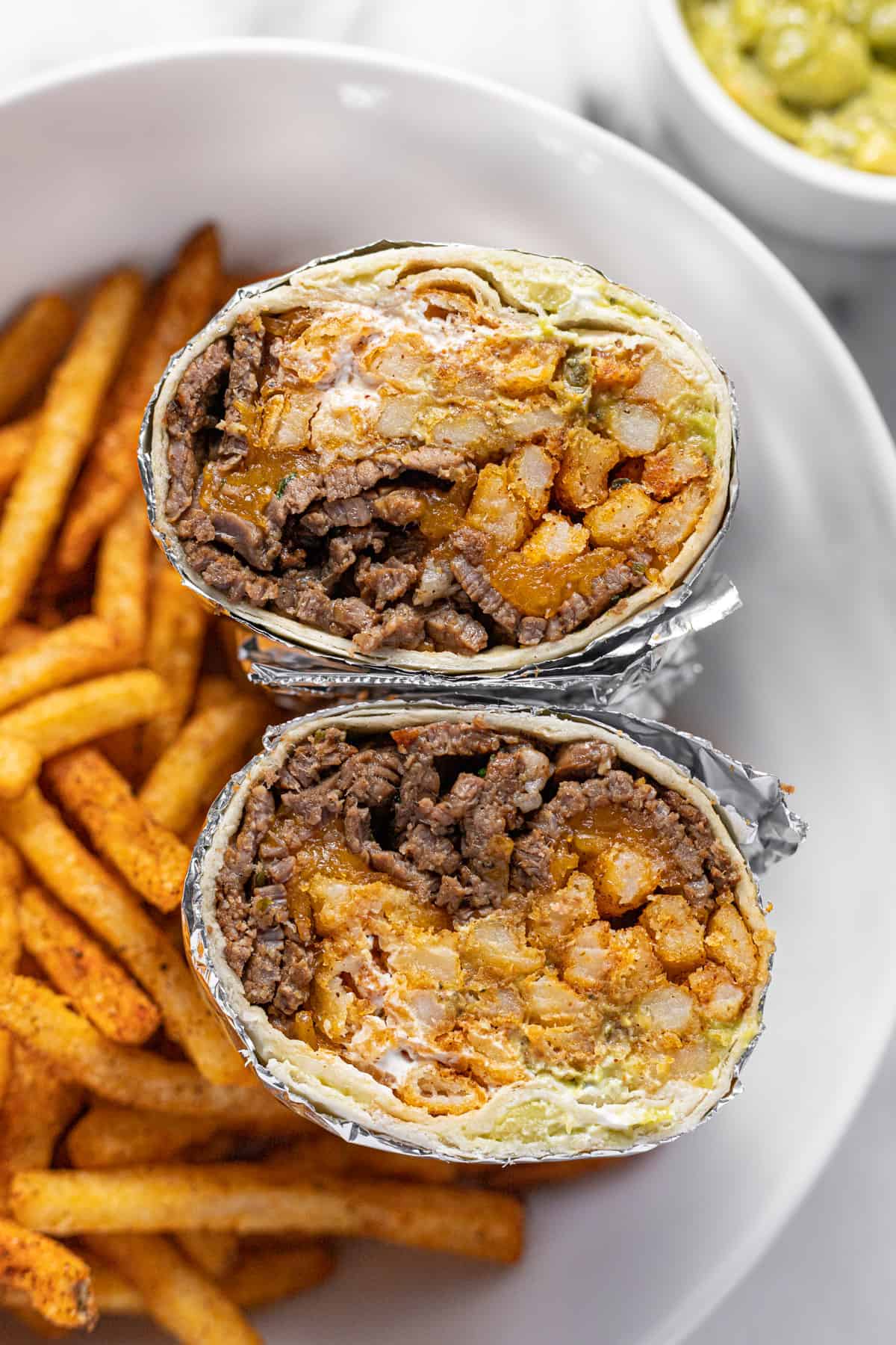 Close up shot of a California burrito cut in half with French fries in the background.