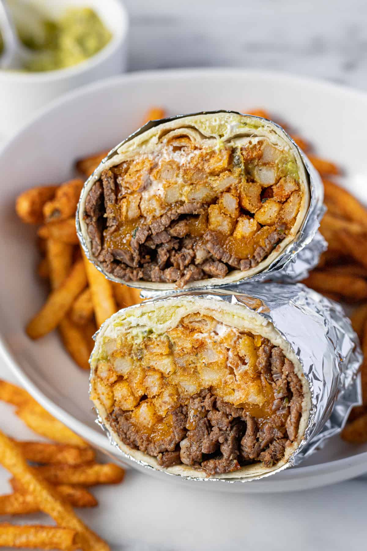A California burrito sliced in half in a bowl of French fries. 