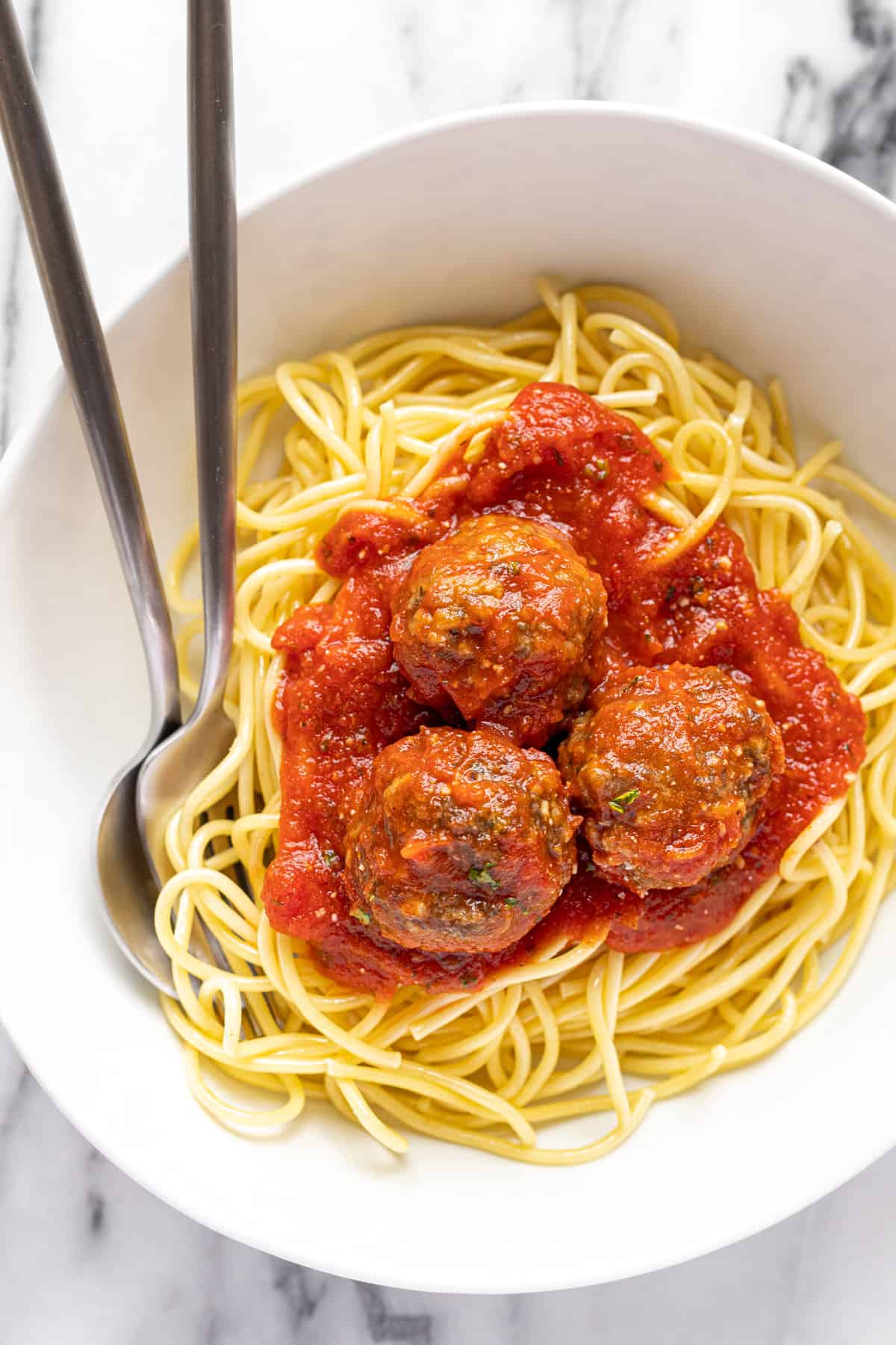 White bowl filled with spaghetti with homemade meatballs. 