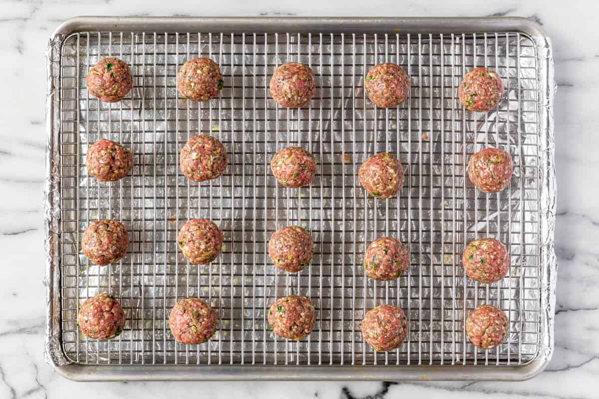 Foil lined baking sheet with a cooling rack on top with homemade uncooked meatballs.