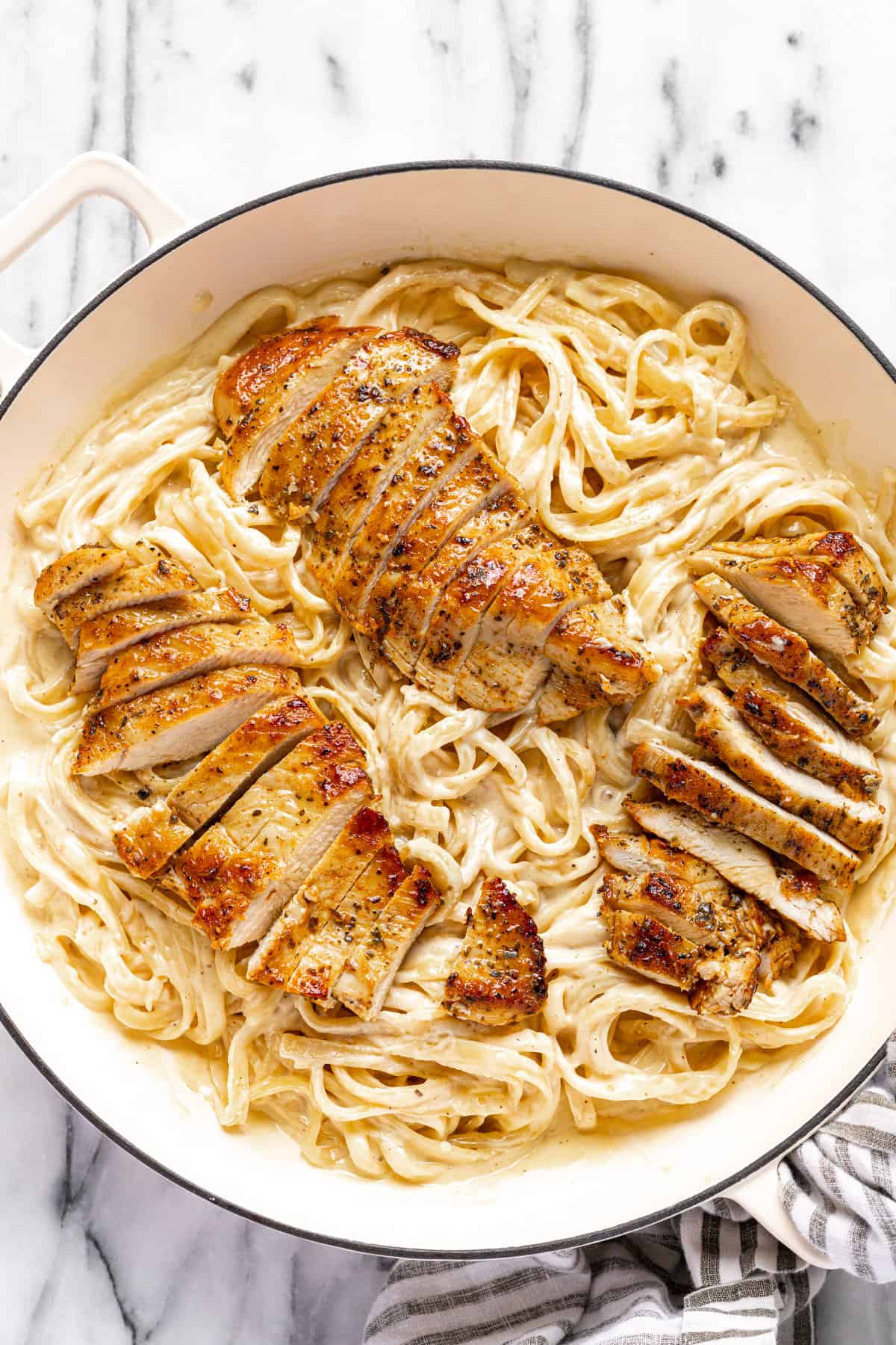 Large white pan filled with homemade fettuccine alfredo topped with chicken.