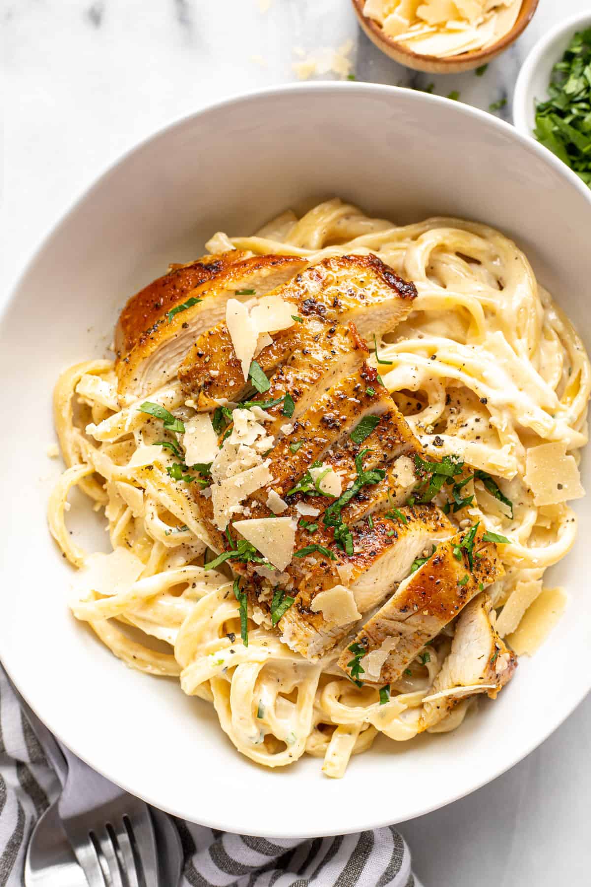 Large white bowl filled with homemade fettuccine alfredo topped with chicken and Parmesan cheese.