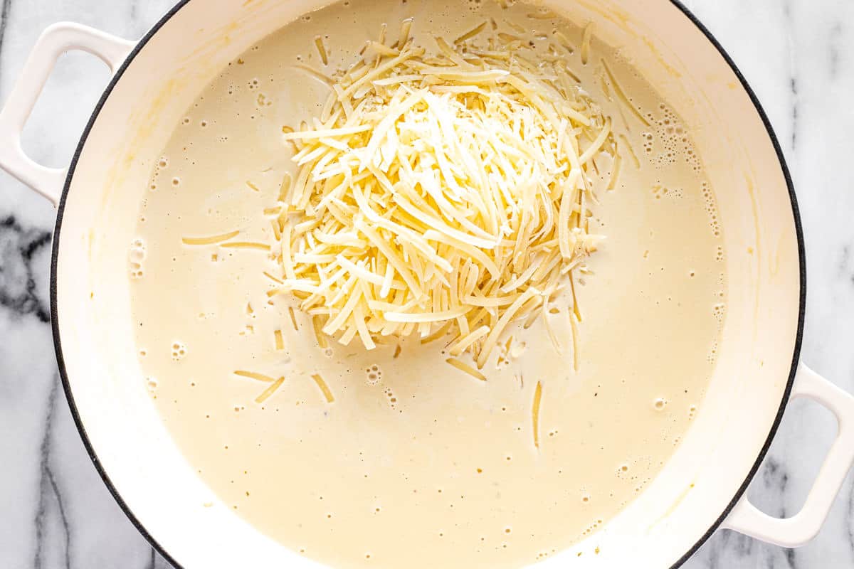 Shredded Parmesan cheese being added to a pan of alfredo sauce.
