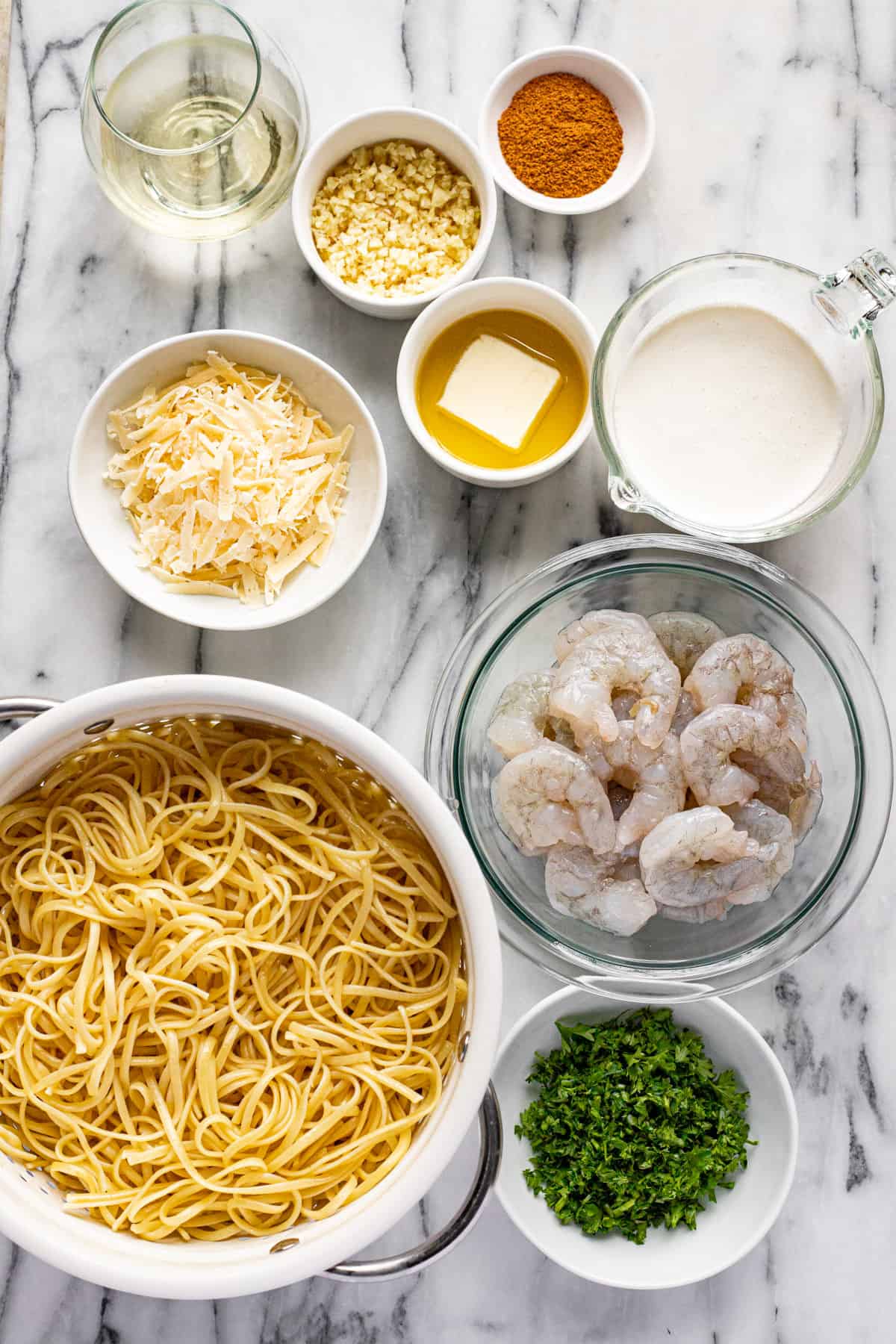 White marble counter top with bowls of ingredients to make Cajun shrimp pasta. 