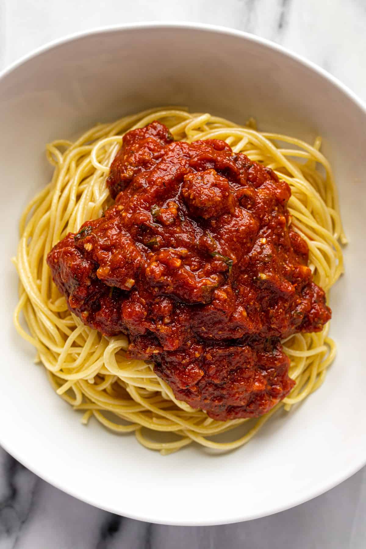 White bowl filled with spaghetti noodles topped with homemade spaghetti sauce. 