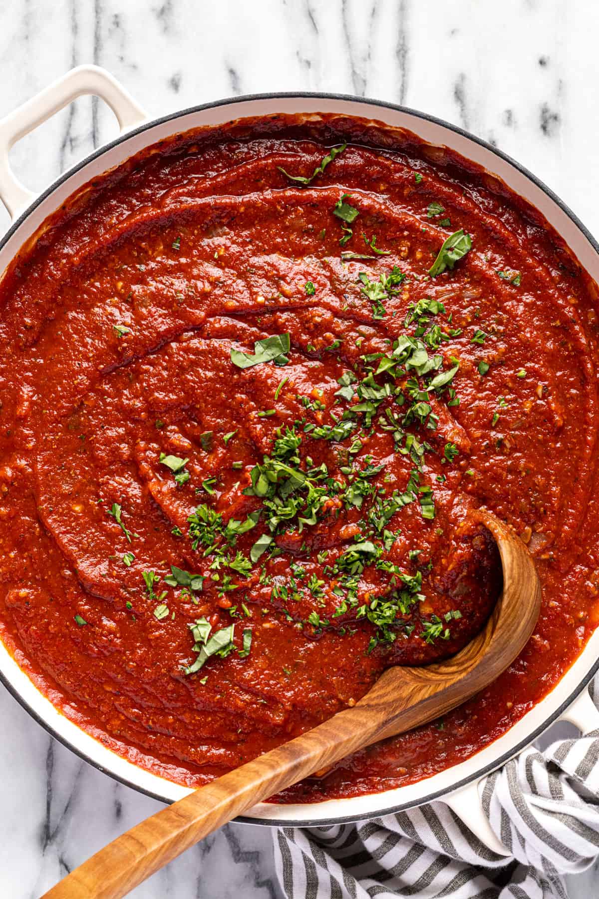 Large white pot filled with homemade meat sauce garnished with fresh herbs.