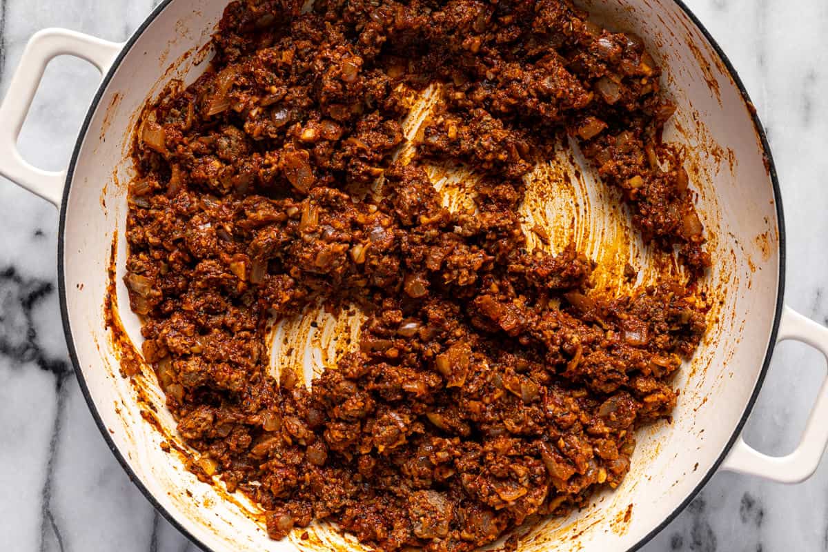 Browned ground beef with herbs, onions, and tomato paste in a large white pot.
