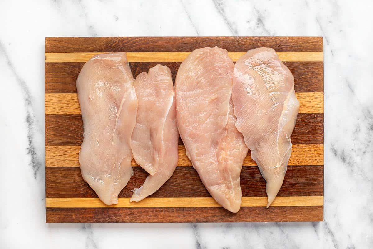 Raw chicken breast sliced on a wooden cutting board.