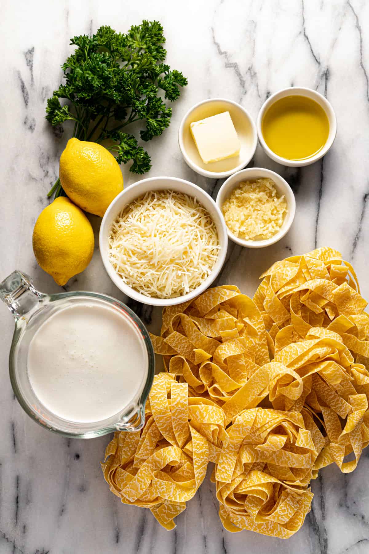 White marble counter top with bowls of ingredients to make lemon pasta.