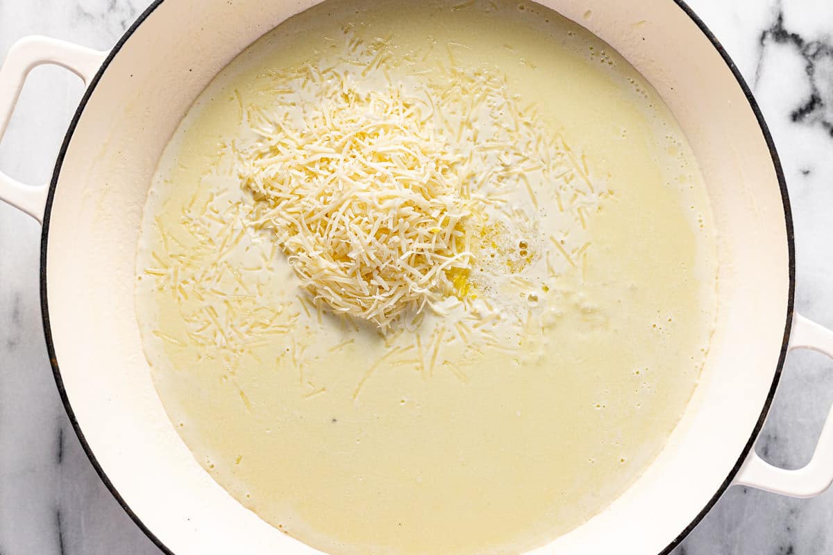 Large white pan filled with creamy lemon sauce with shredded Parmesan being added. 