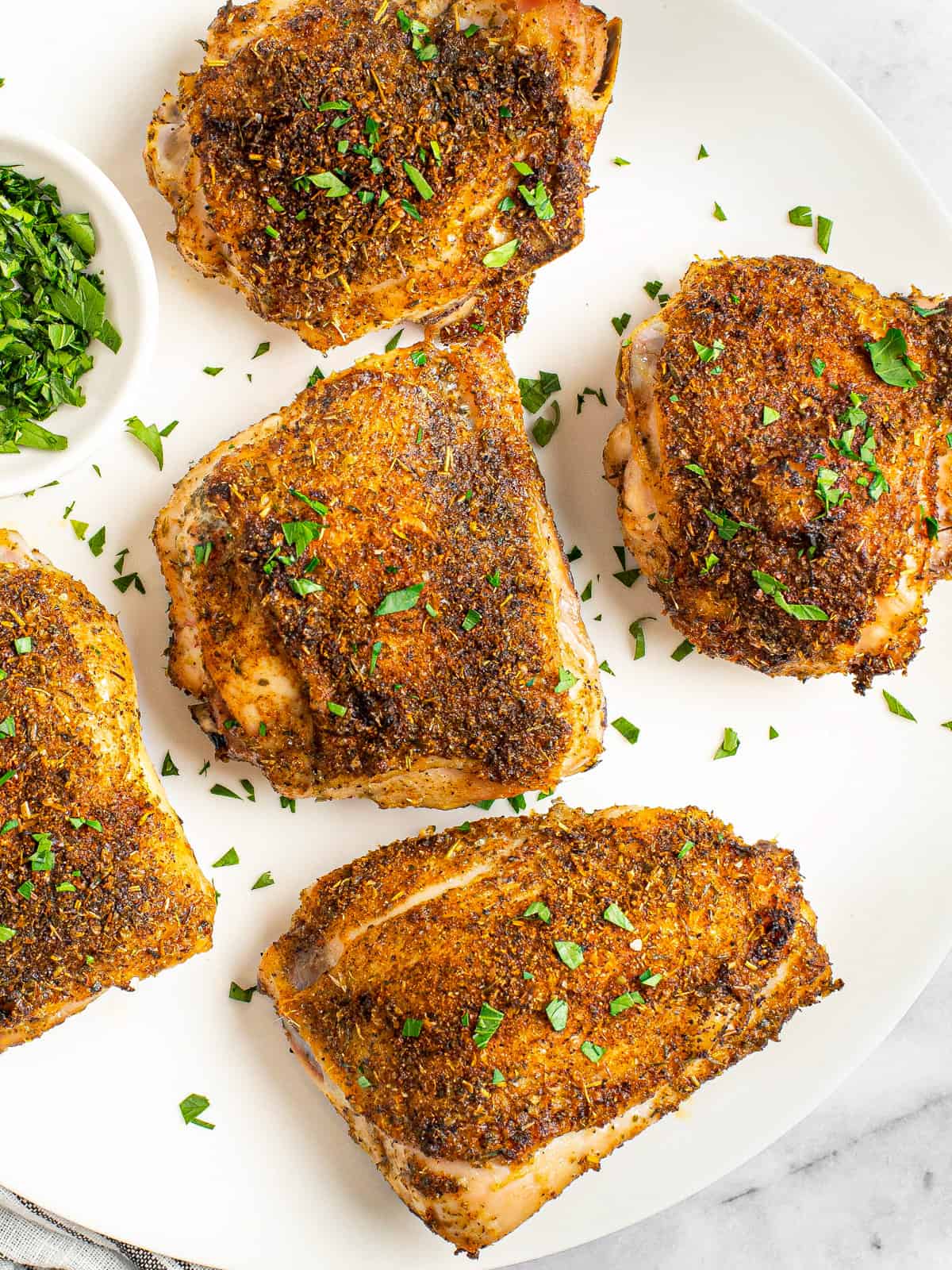 White plate filled with oven baked chicken thighs garnished with fresh parsley.