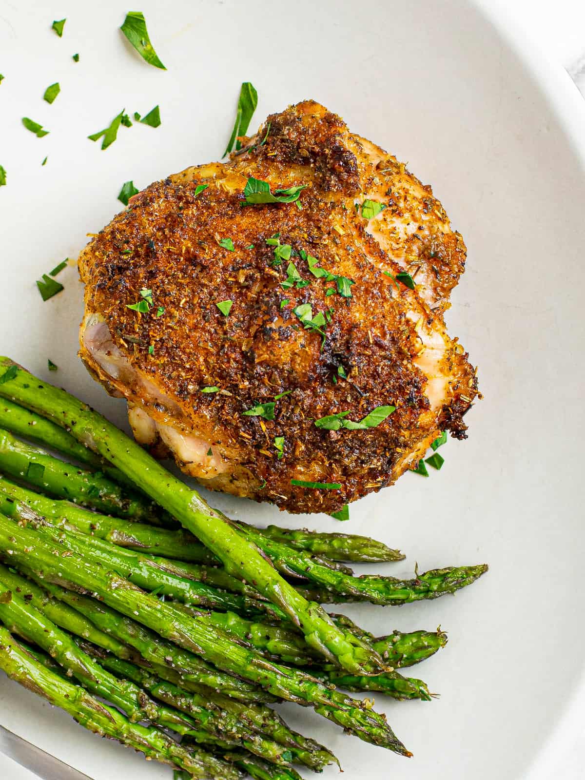 A baked chicken thigh with asparagus on a large white plate.