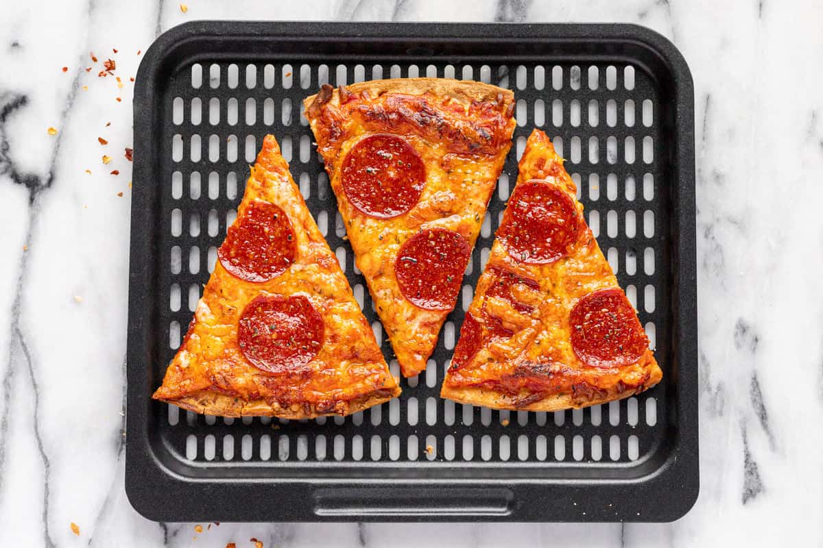 Black air fryer tray with slices of pepperoni pizza on it.