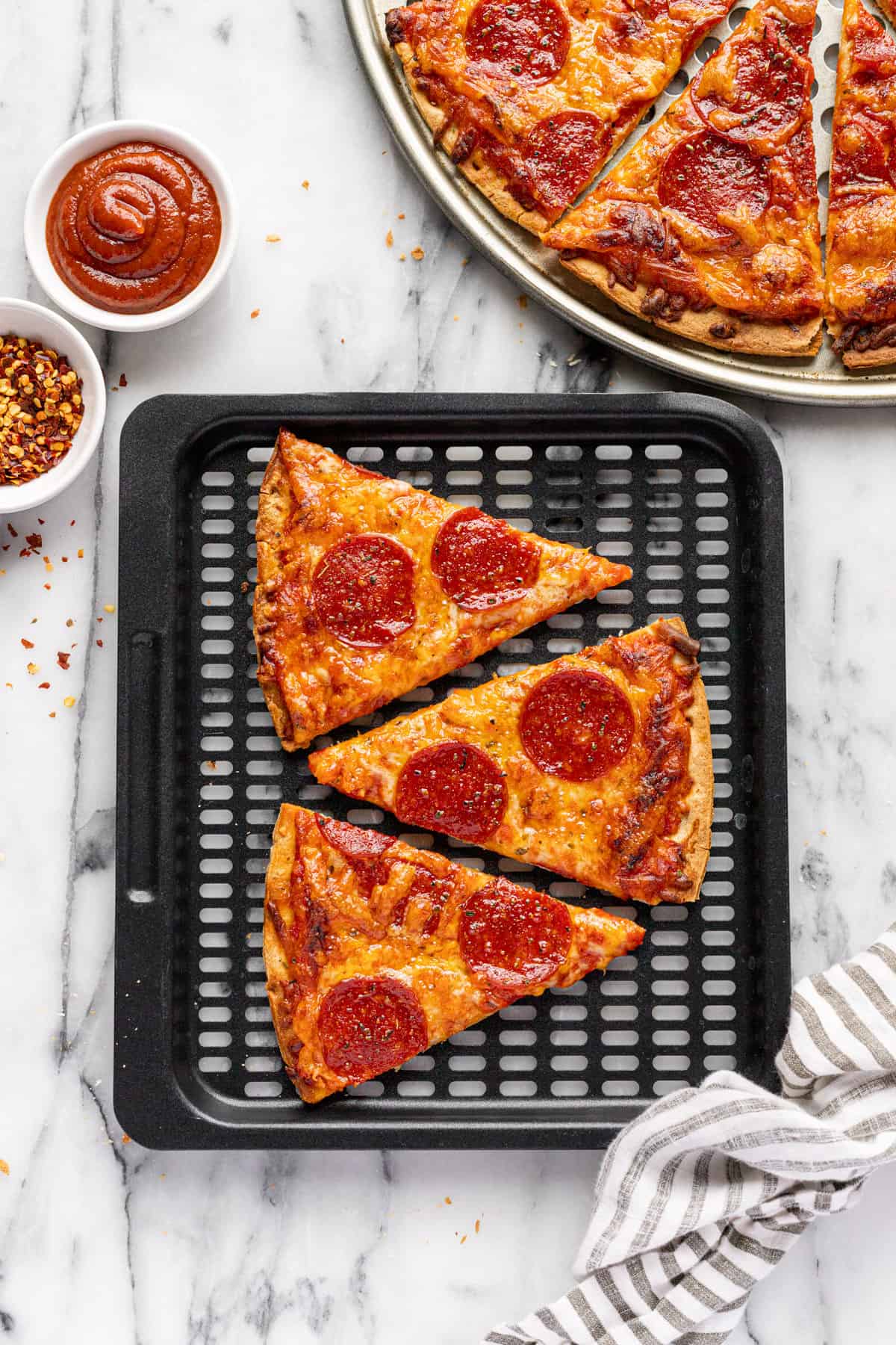 Air fryer tray with three slices of pepperoni pizza next to a pan of pizza.
