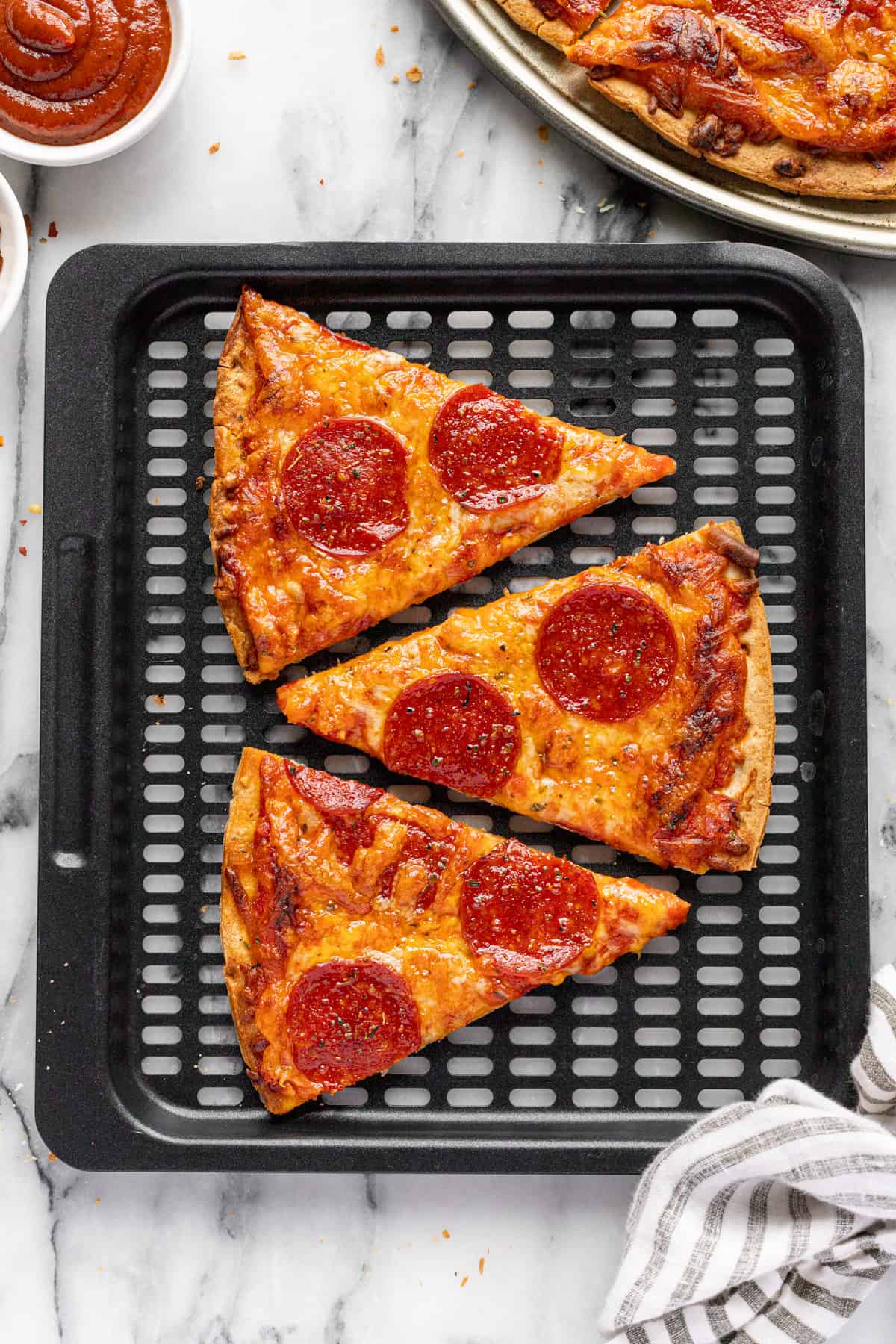 Black air fryer tray with slices of pepperoni pizza on it.
