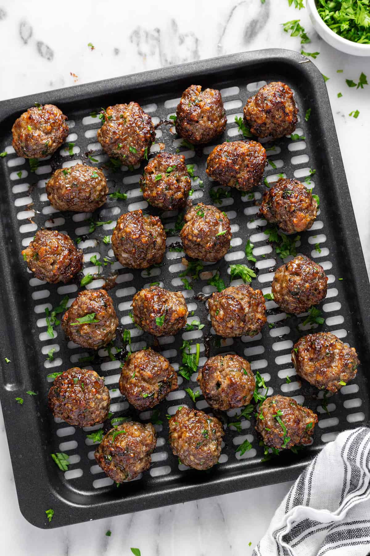 Air fryer tray with freshly cooked Italian meatballs garnished with parsley.