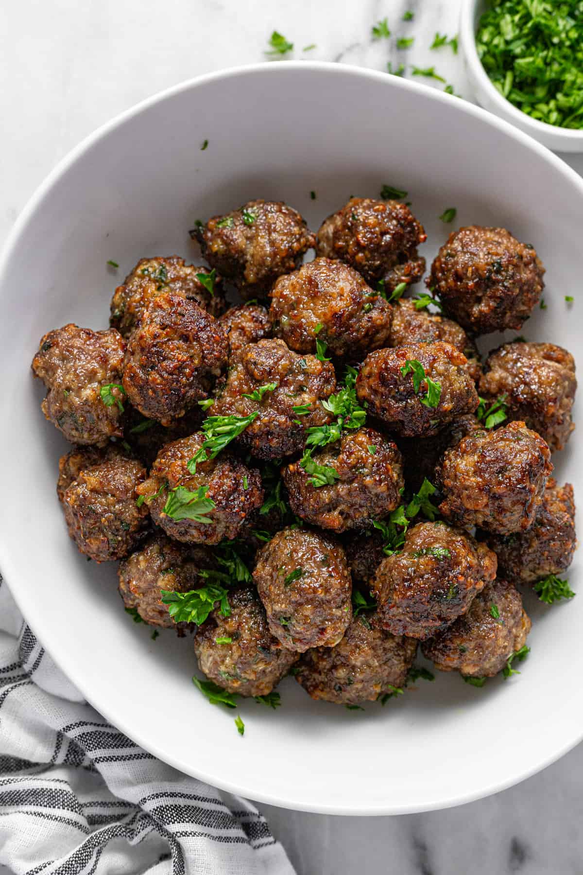 White bowl filled with freshly cooked air fryer meatballs garnished with parsley. 