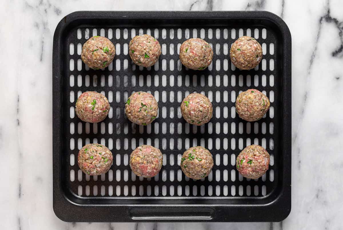 Air fryer tray with raw meatballs on it.
