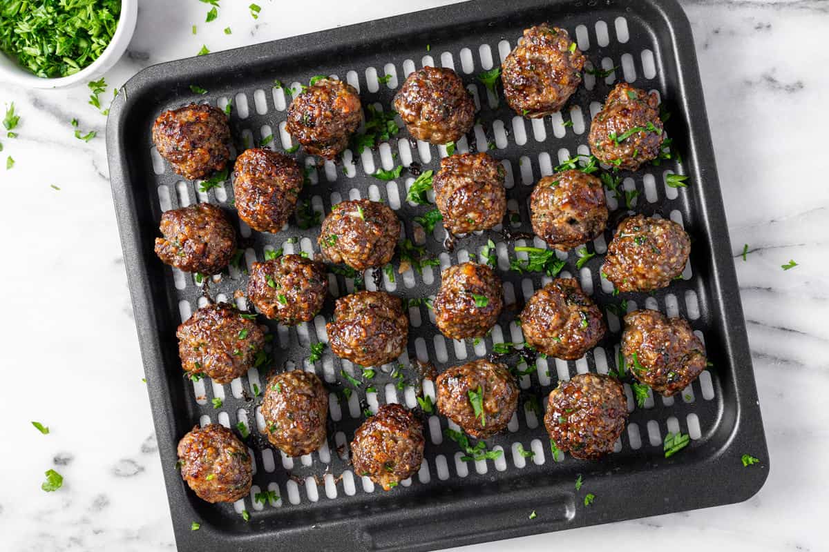 Black air fryer tray filled with homemade Italian meatballs garnished with parsley. 