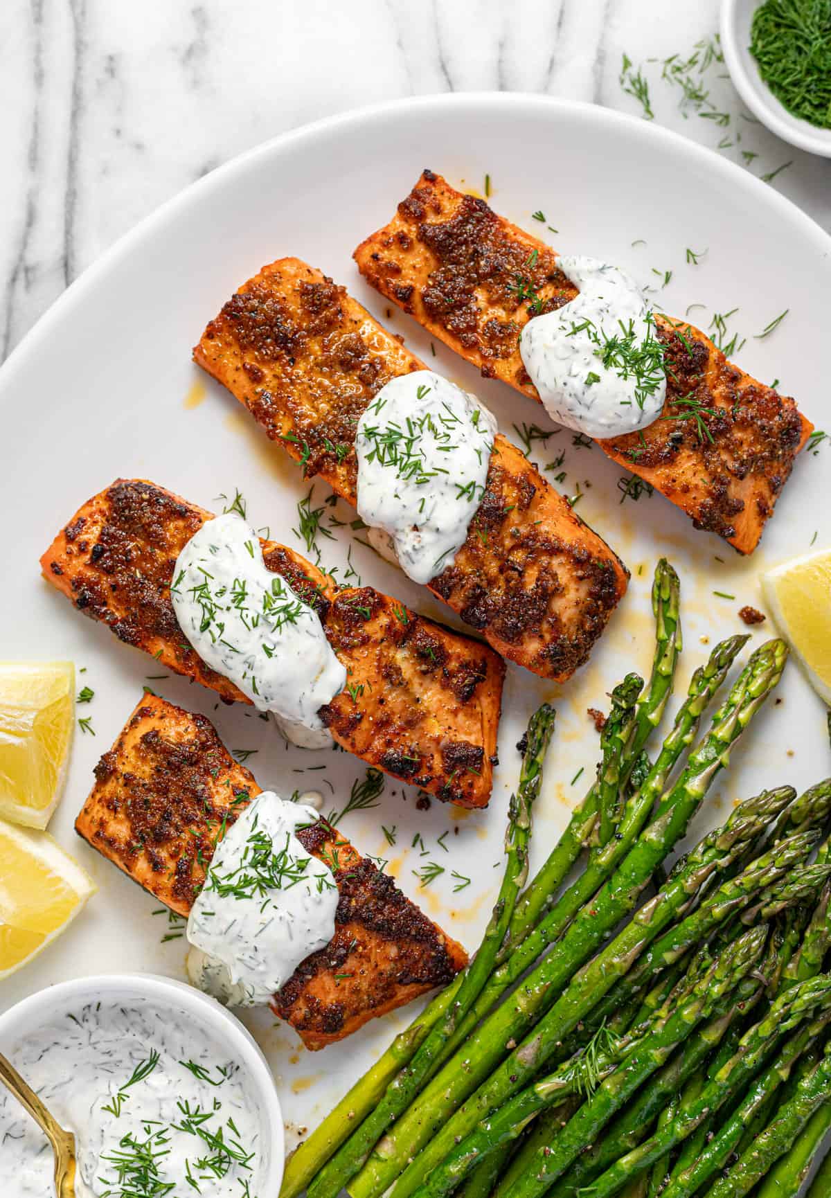 White serving platter with 4 fillets of salmon drizzled with dill sauce. 