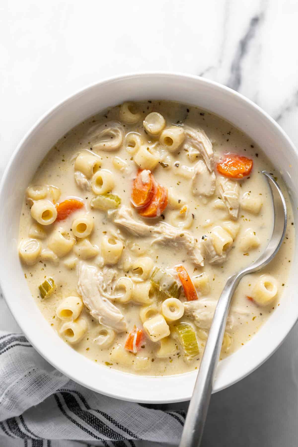Bowl of creamy chicken noodle soup with a spoon in it.