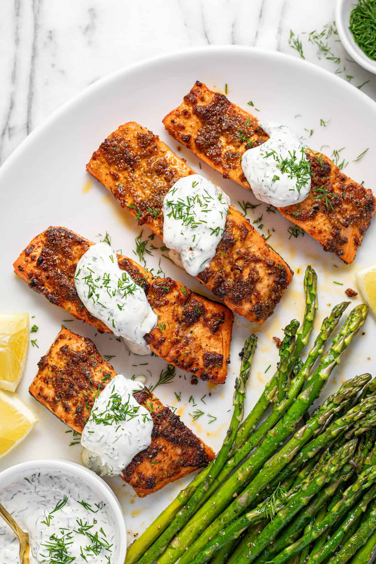 Large white platter filled with salmon, asparagus, and creamy dill sauce. 