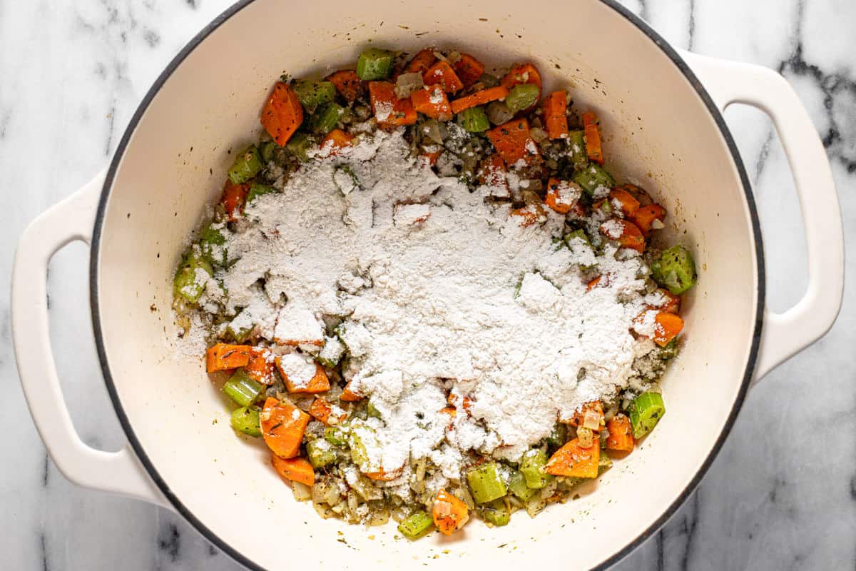 Large pot with sauteed veggies sprinkled with flour. 