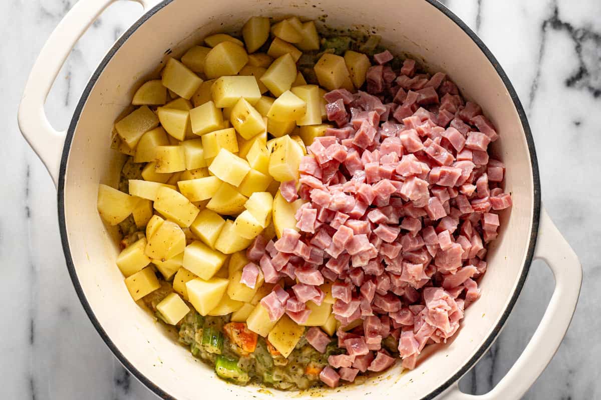 Diced potatoes and diced ham added to a large pot of sauteed veggies.
