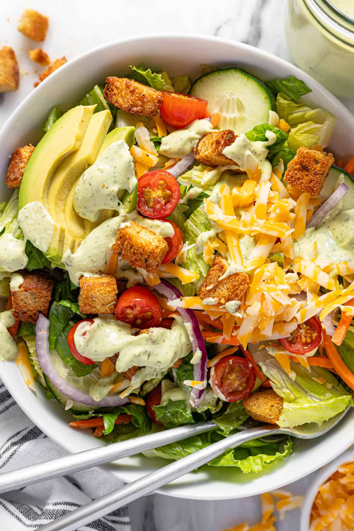 Big bowl filled with greens, veggies, cheese, and croutons, drizzled with creamy dressing.