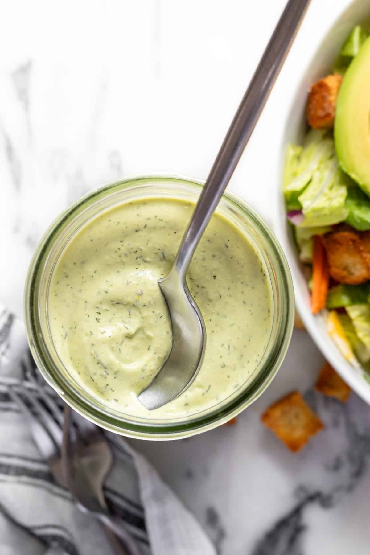 Wide-mouth mason jar filled with creamy avocado lime ranch dressing with a spoon in it.