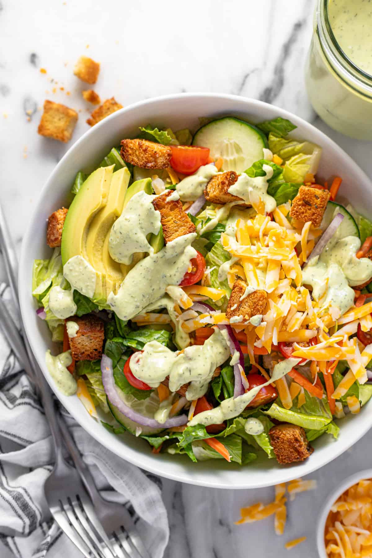 Big bowl filled with greens, veggies, cheese, and croutons, drizzled with creamy dressing.