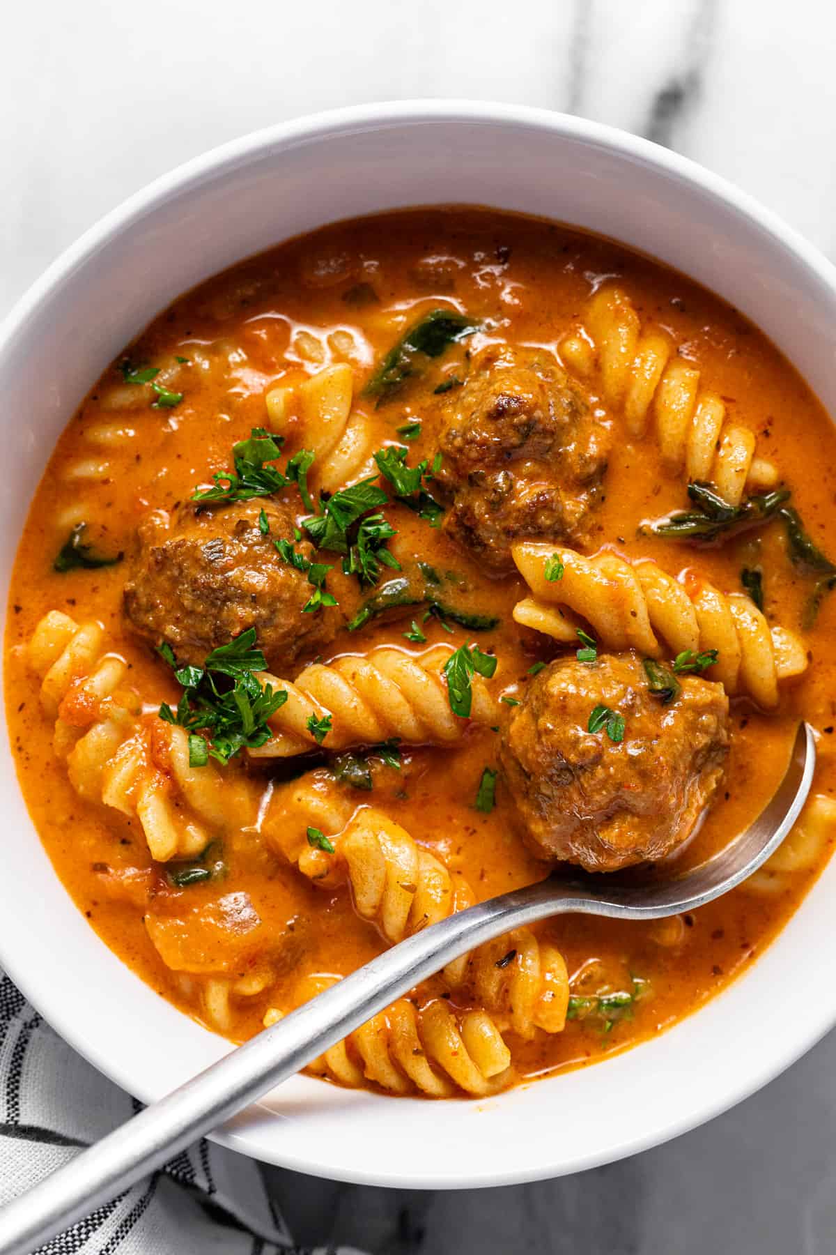 White bowl filled with creamy homemade Italian meatball soup garnished with parsley. 
