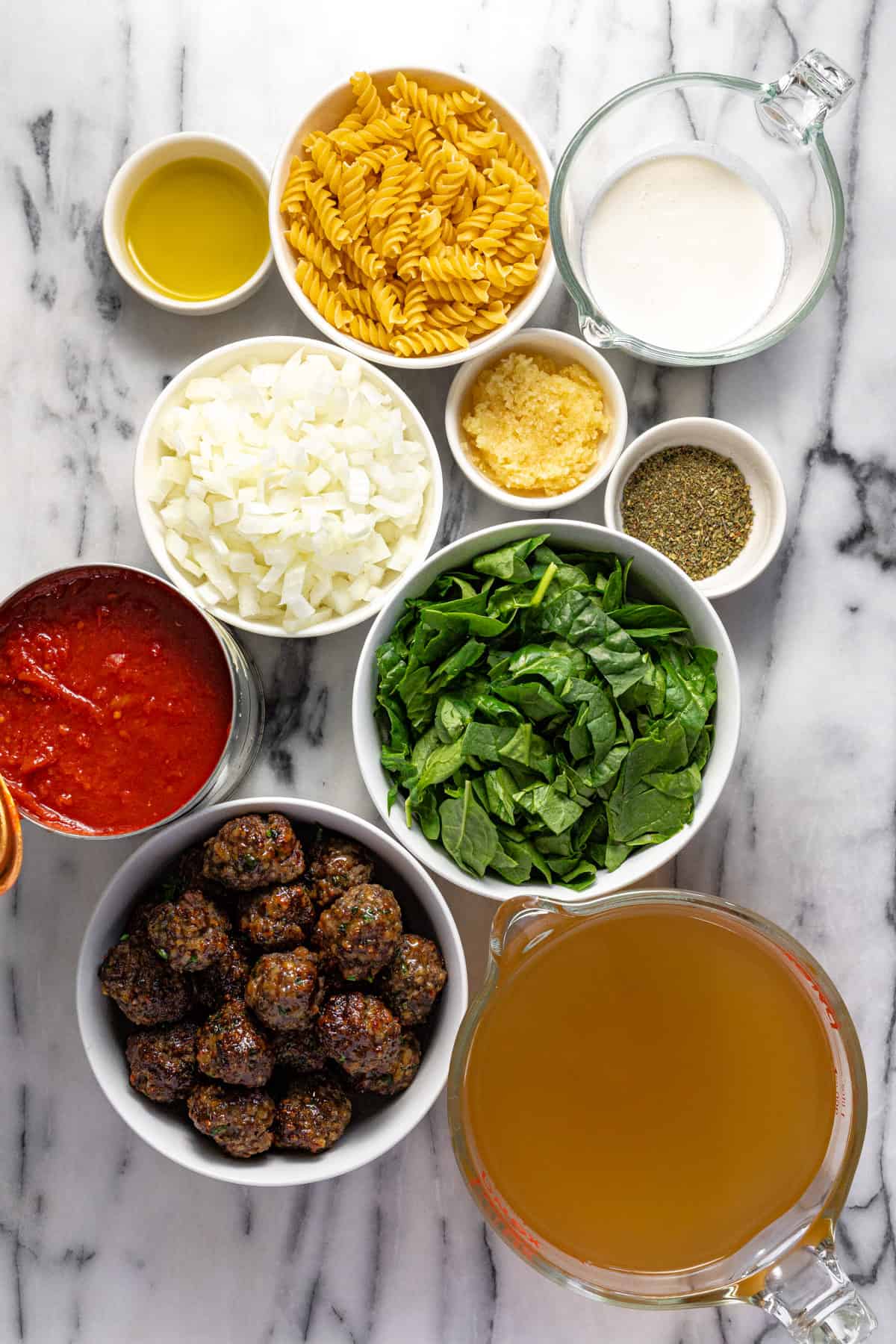 White marble counter top with bowls of ingredients to make creamy meatball soup.