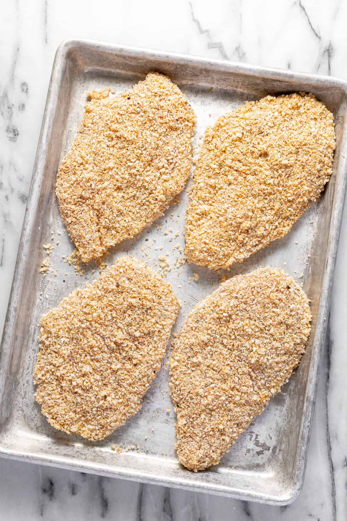 Small baking sheet with four Parmesan crusted chicken breasts on it, ready to be pan-fried. 