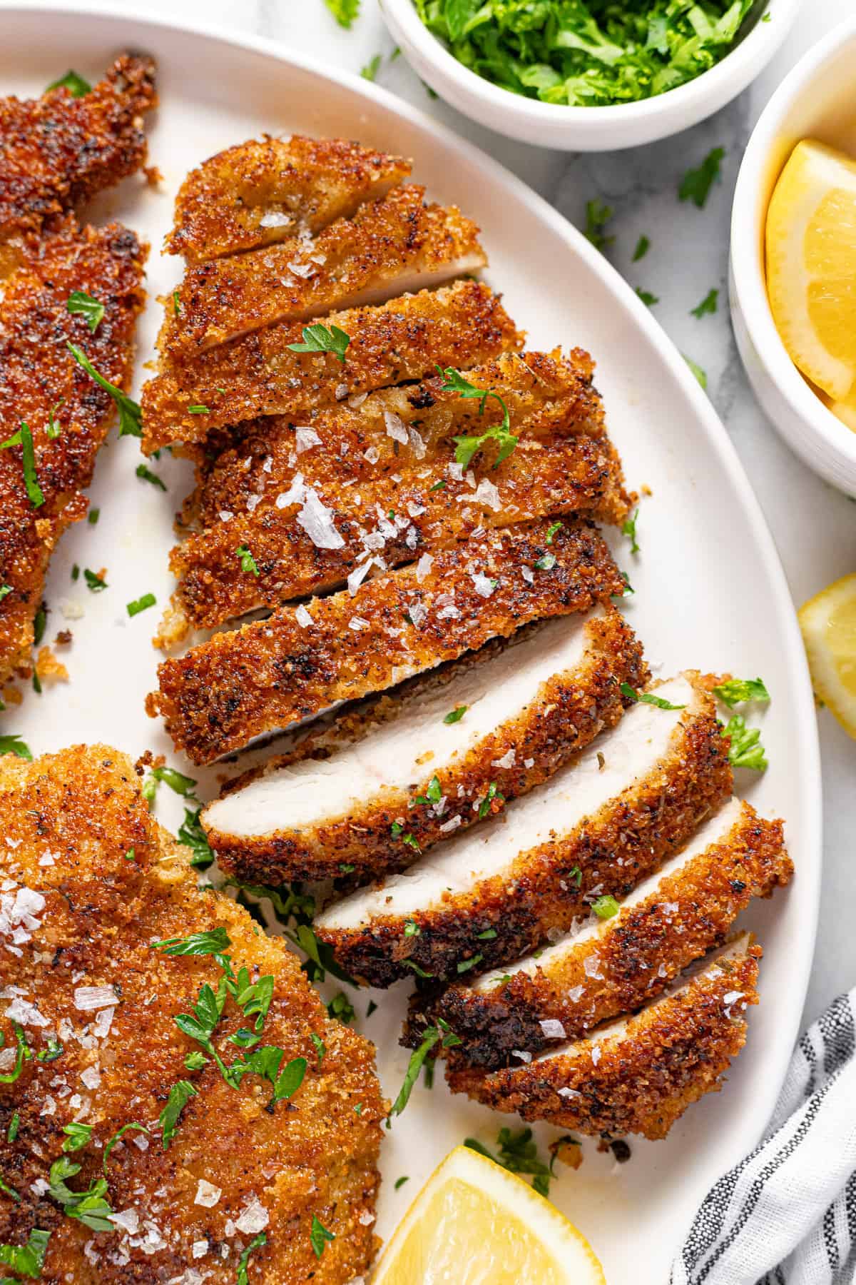 A sliced Parmesan crusted chicken breast on a white plate garnished with fresh parsley. 