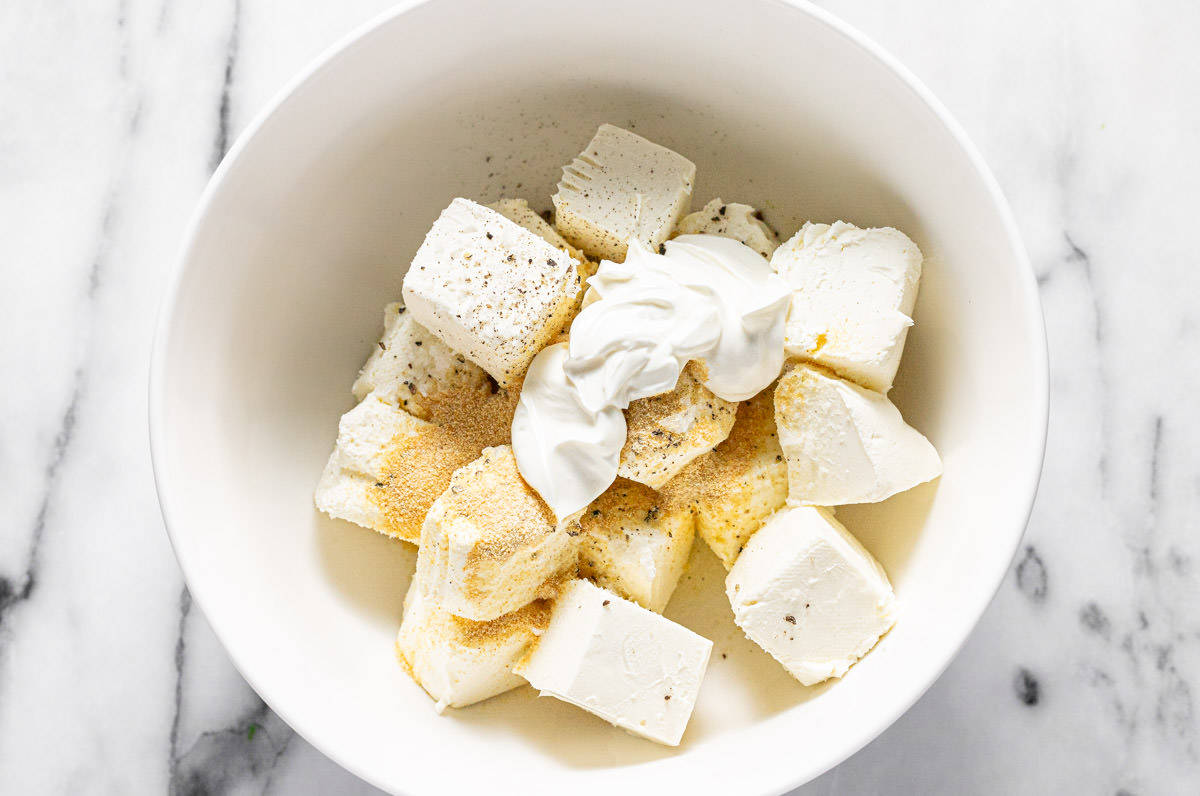 Large bowl filled with cubed cream cheese, sour cream, and spices. 