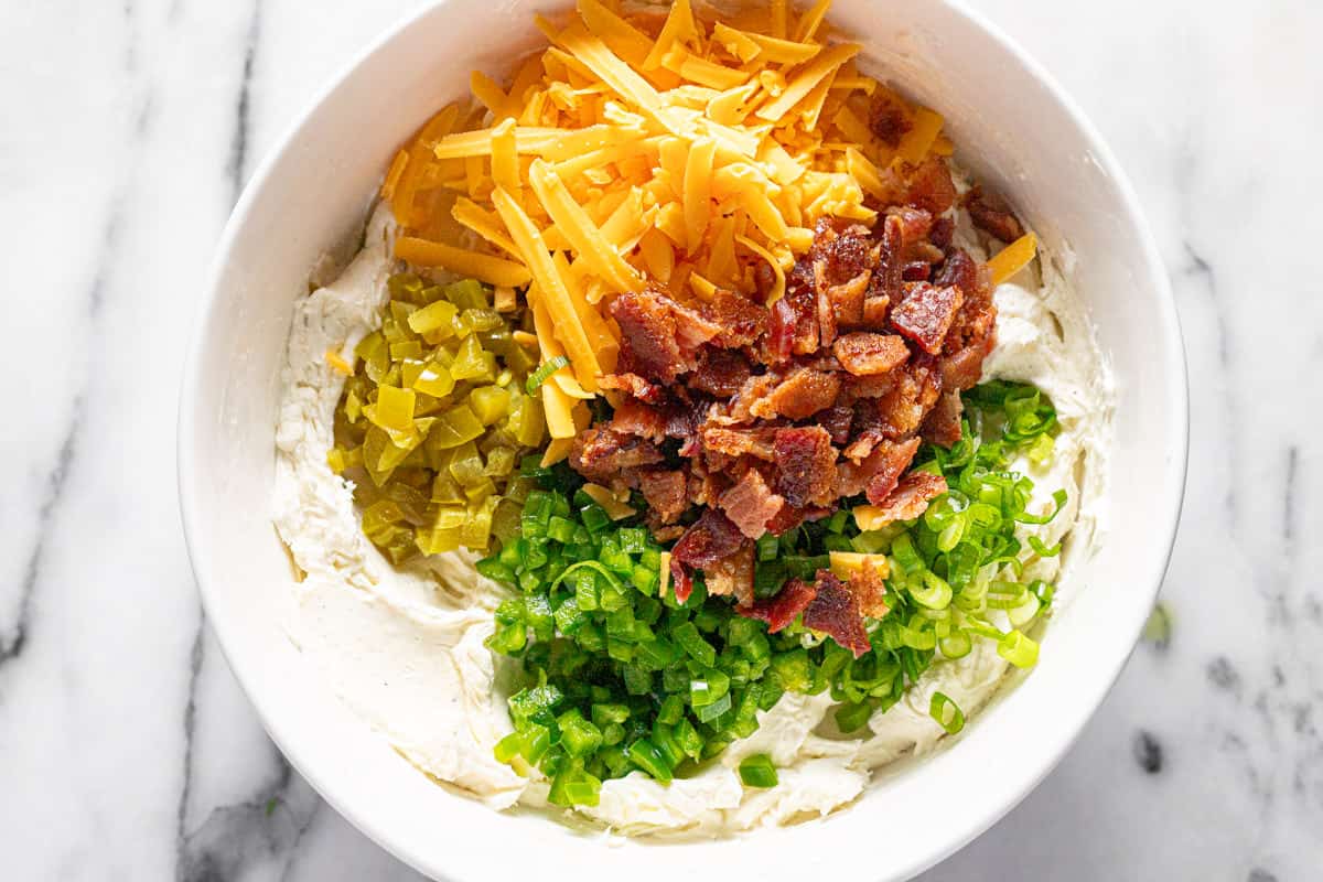 Shredded cheese, bacon, green onions, and jalapenos added to a large bowl of cream cheese and sour cream. 