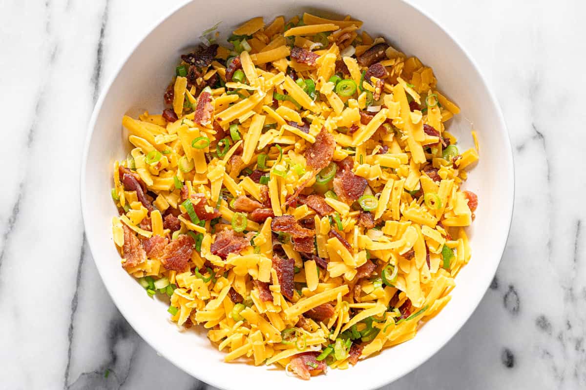 A large bowl filled with shredded cheese, bacon, and green onion for coating the cheese ball. 