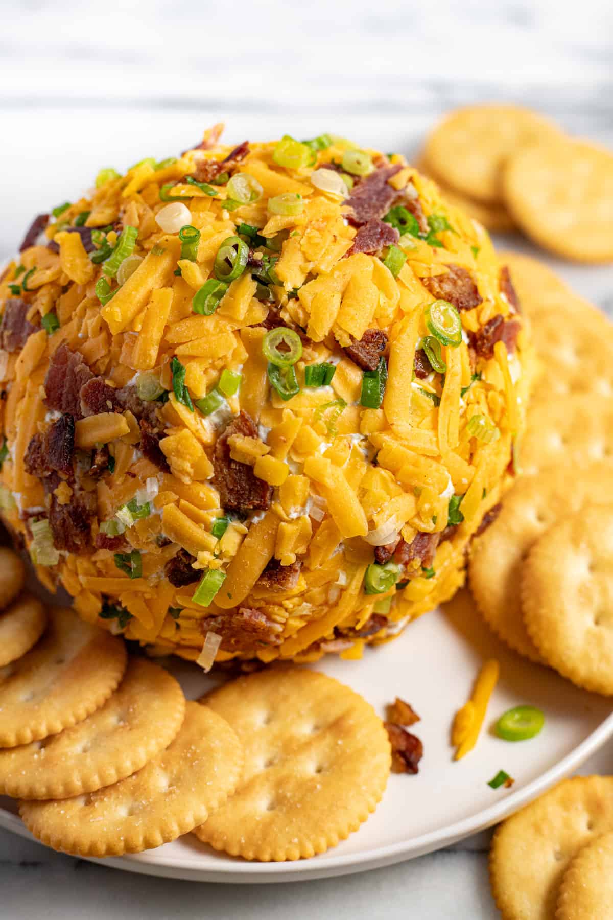 A jalapeno popper cheese ball on a round plate with Ritz crackers. 