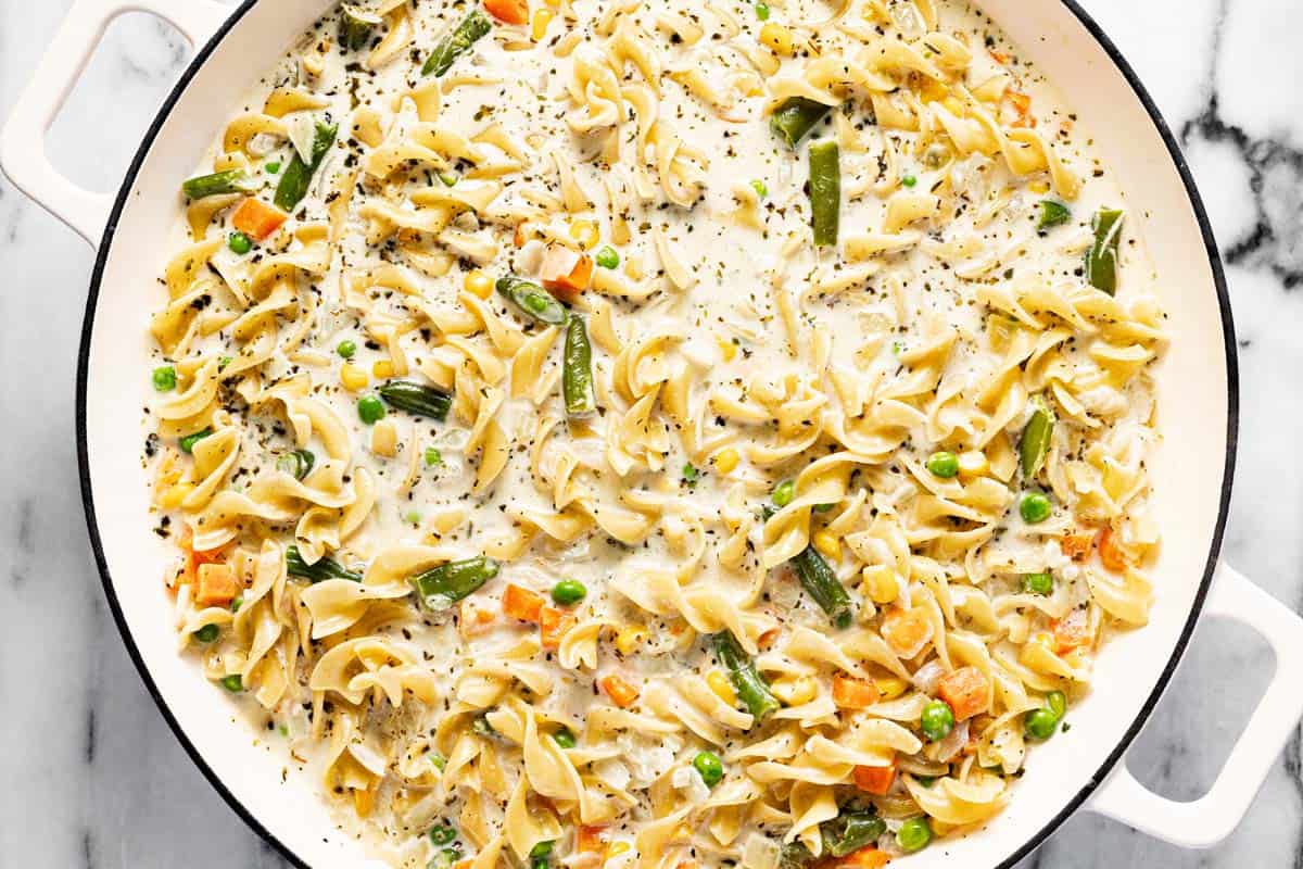 Large saute pan filled with cream sauce, egg noodles, and veggies. 