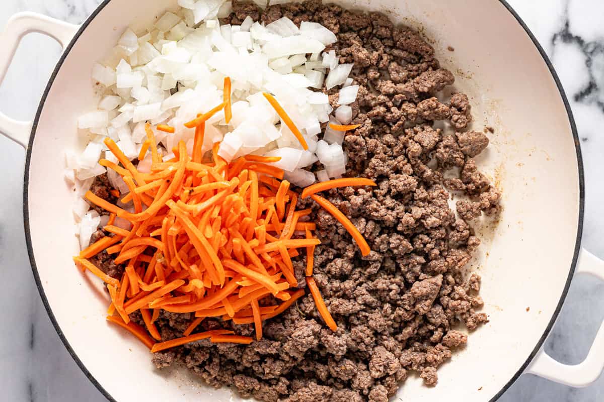 Browned ground beef, diced onion, and matchstick carrots in a large pan. 
