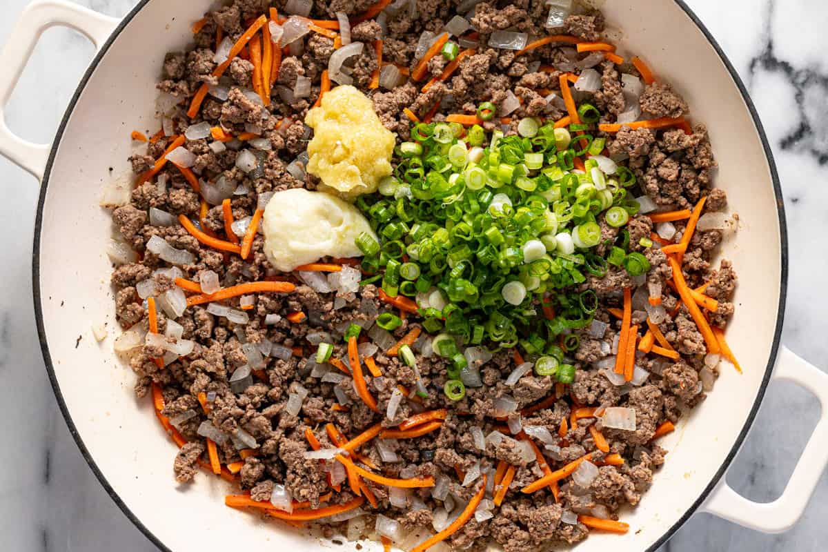 Ground beef with sauteed veggies in a large pan with green onions, garlic paste, and ginger paste.