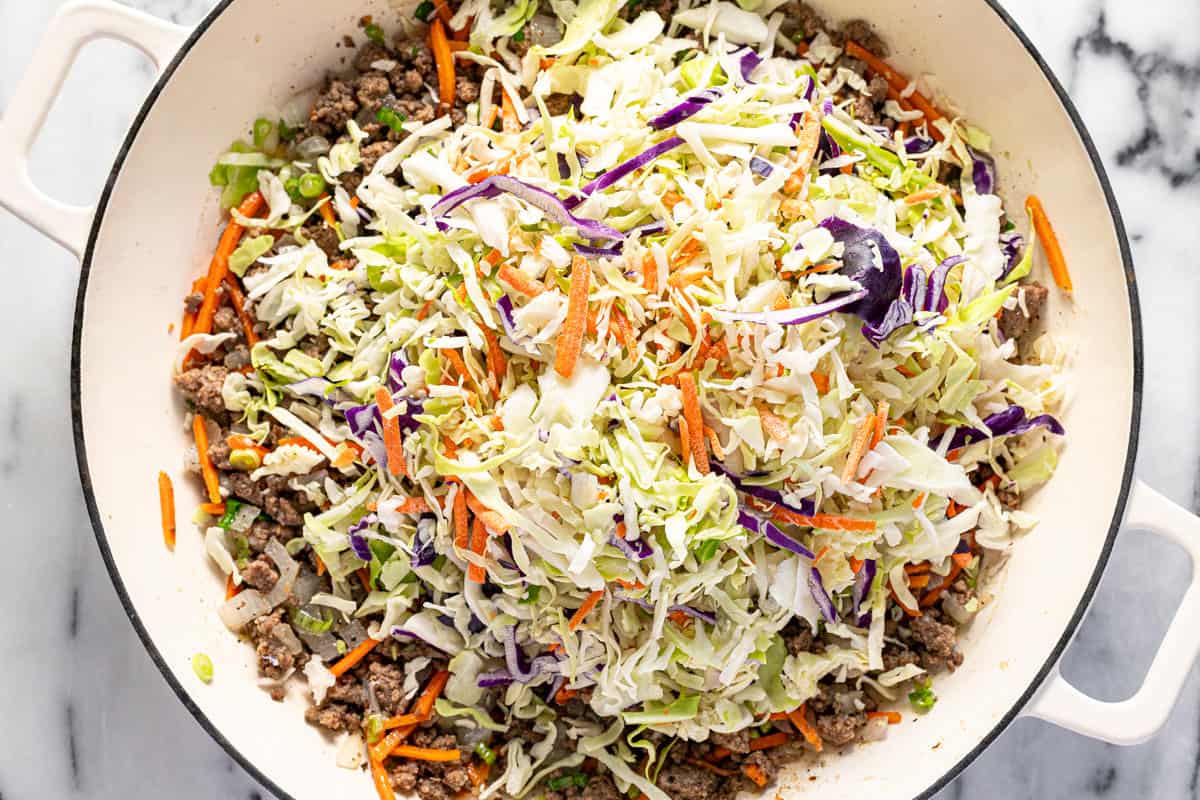 A pile of cabbage being added to a large pan of ground beef, veggies, garlic, and ginger.