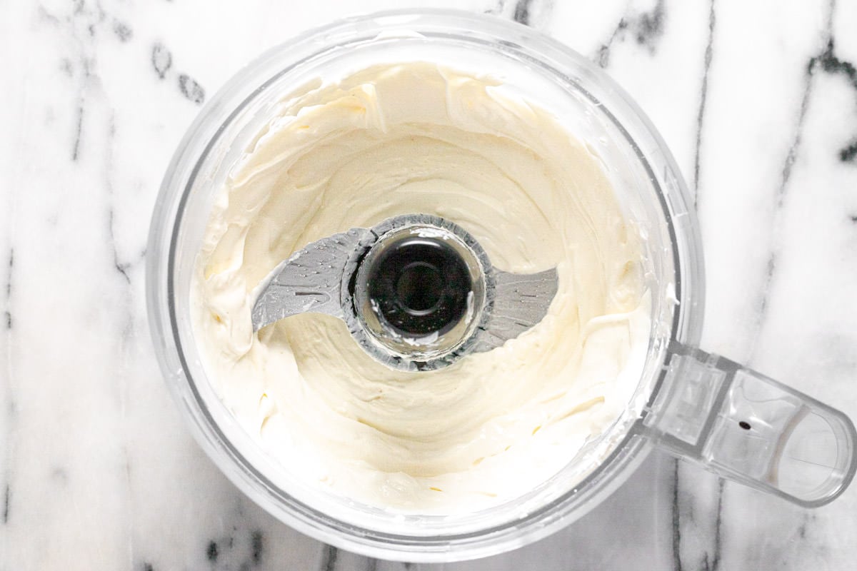 Food processor filled with smooth cream cheese and sour cream. 
