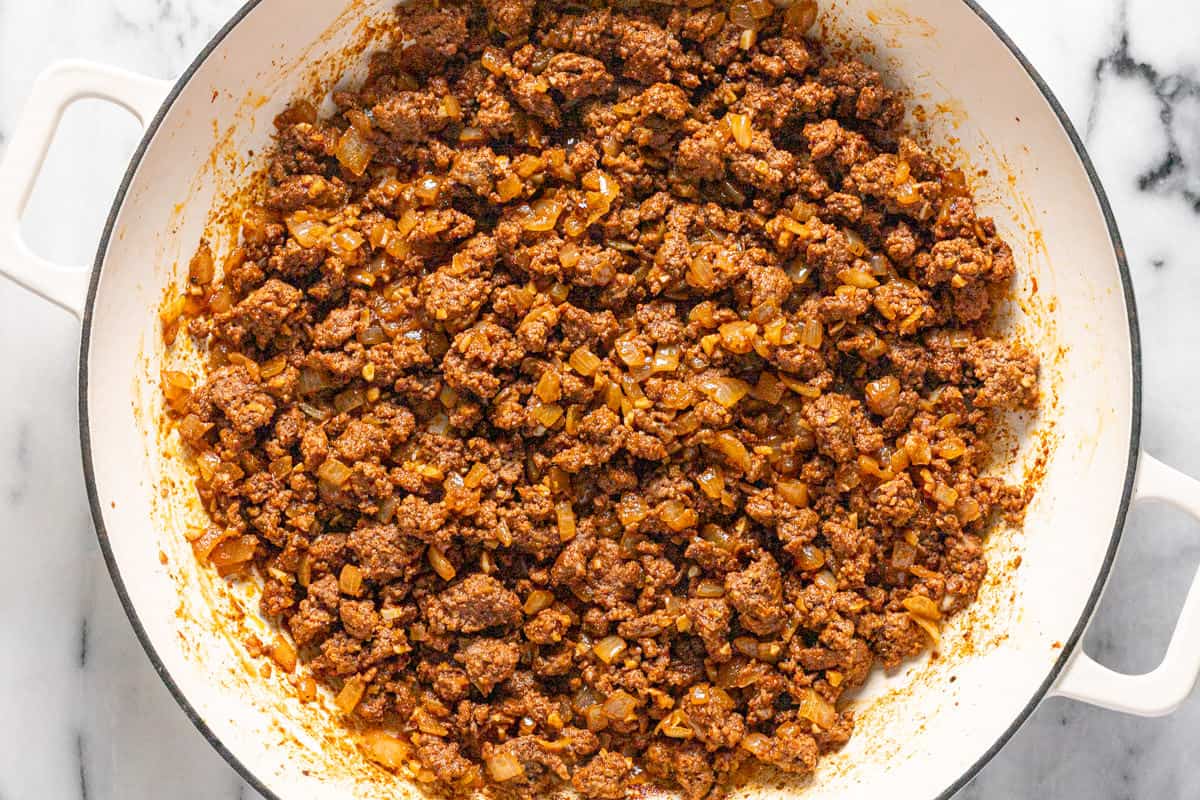 Large sauté pan filled with browned ground beef, onions, and spices.
