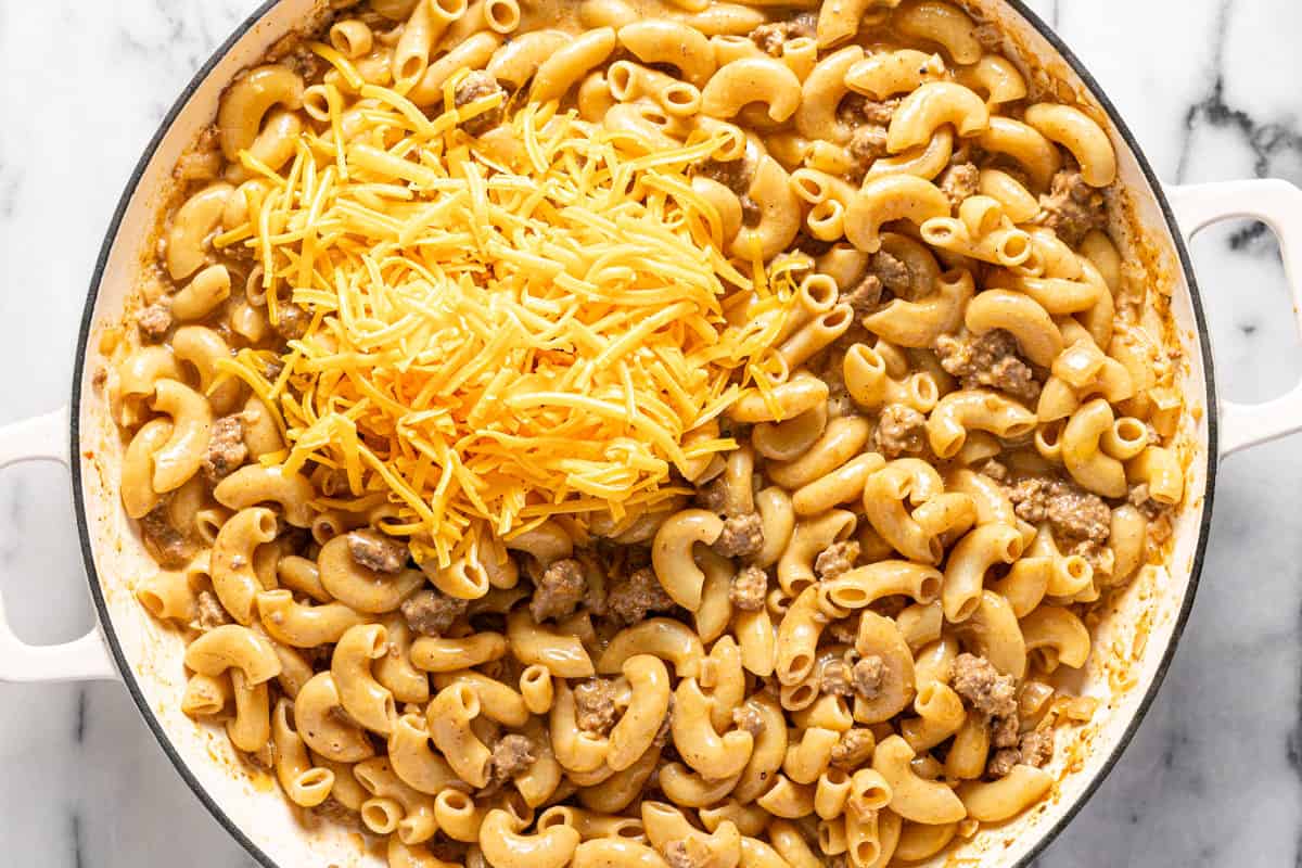 Large pan filled with cooked macaroni noodles and ground beef with shredded cheese on top. 