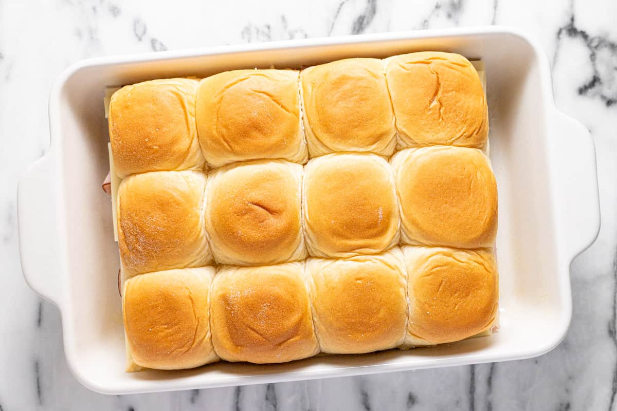 Large baking dish filled with assembled ham and cheese sliders on Hawaiian rolls. 