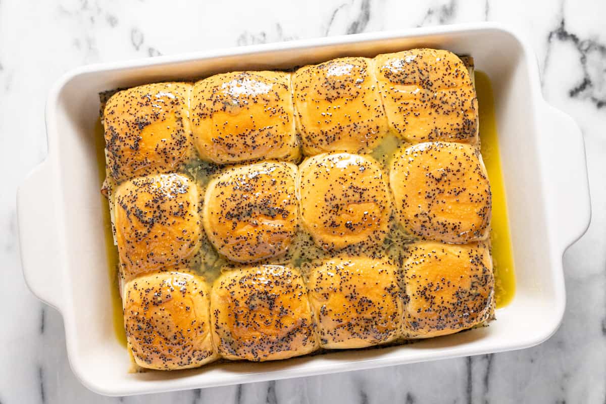 Ham and cheese sliders in a large baking dish with poppyseed butter sauce poured over them. 