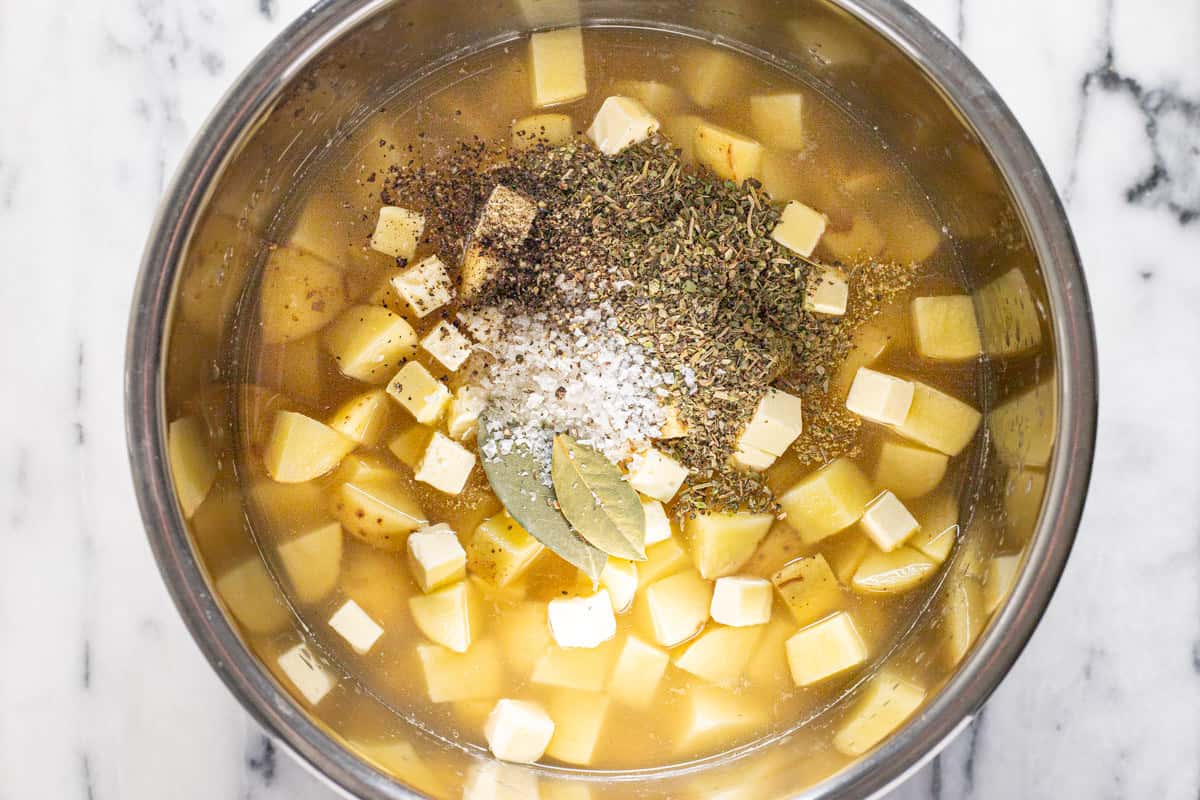 Instant pot insert filled with diced potatoes, diced butter, and dried herbs.