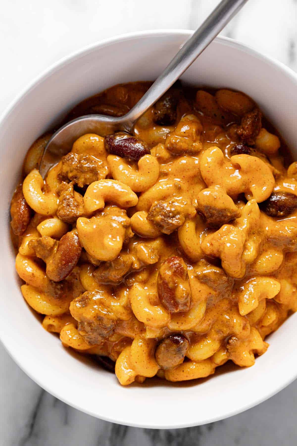 White bowl filled with creamy chili mac with a spoon. 